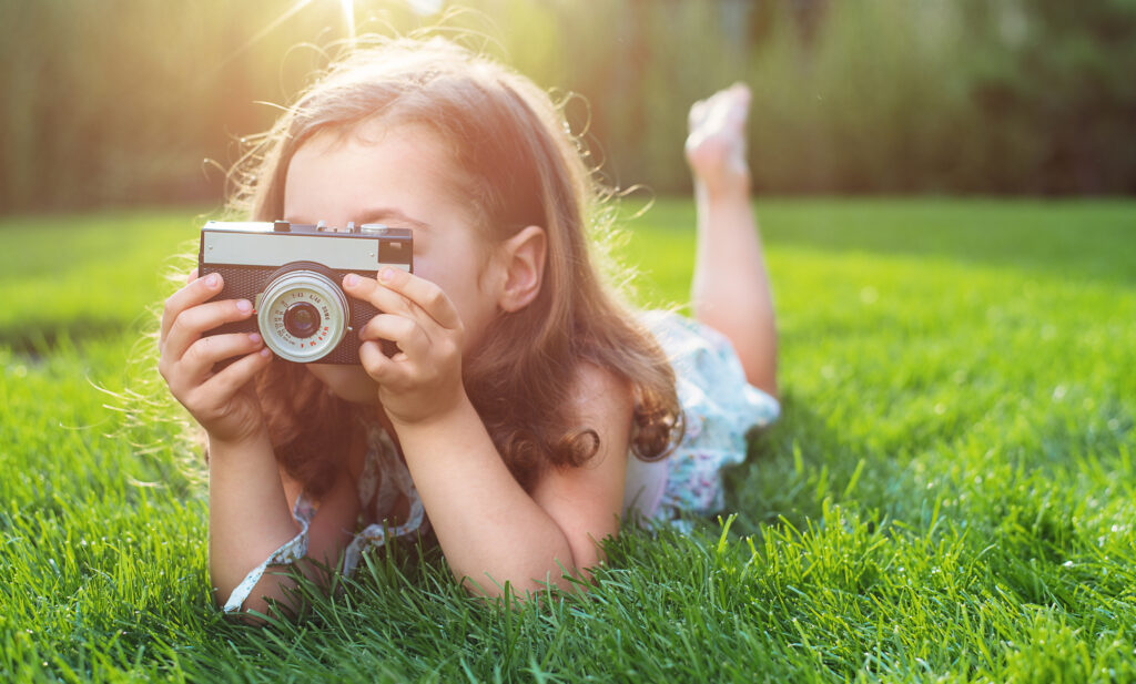 Cute little childl lying on green lawn and taking a picture