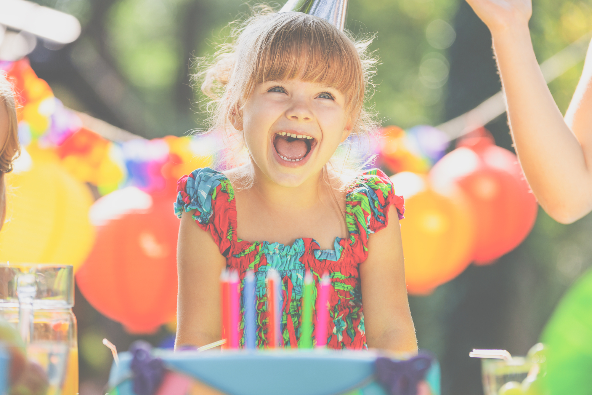 Smiling girl in colorful dress blowing out the candles on a birthday cake during party